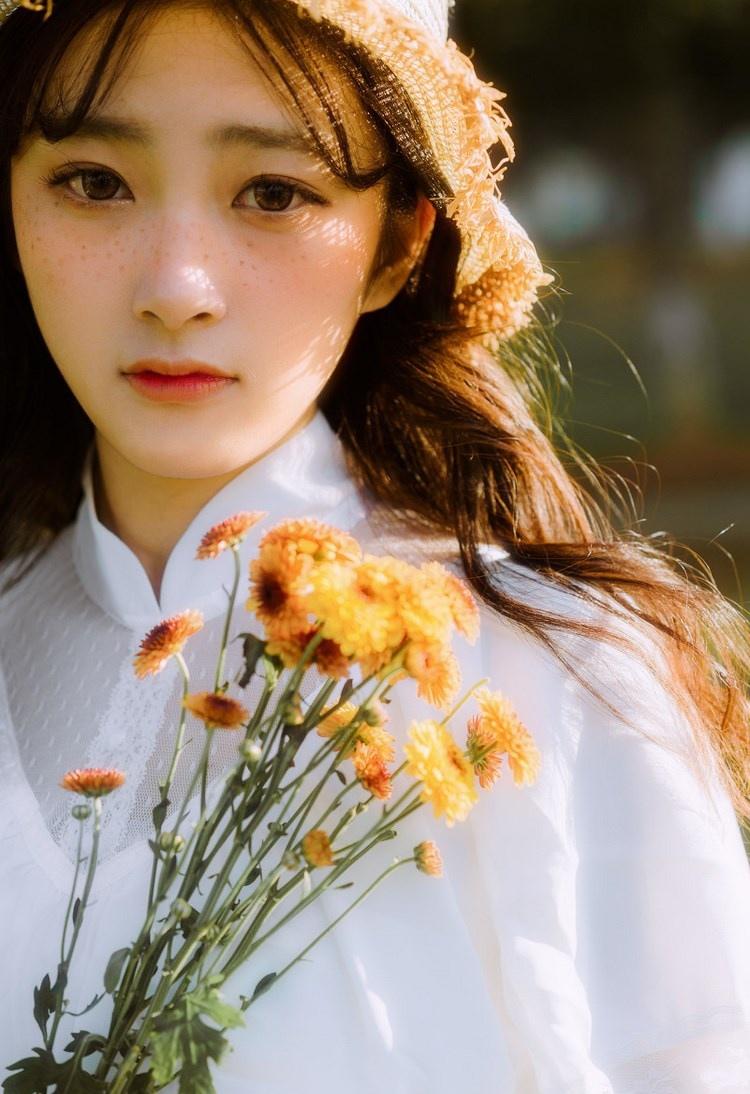 文藝美女潔白長(zhǎng)裙?jié)饷芫戆l(fā)手捧鮮花叢林寫(xiě)真圖片