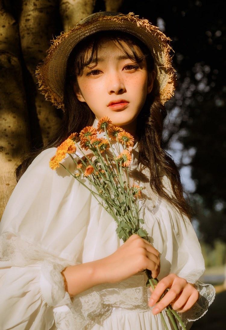 文藝美女潔白長(zhǎng)裙?jié)饷芫戆l(fā)手捧鮮花叢林寫(xiě)真圖片