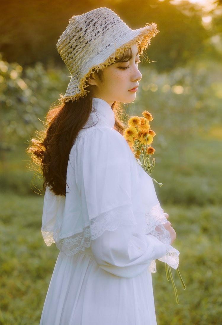 文藝美女潔白長(zhǎng)裙?jié)饷芫戆l(fā)手捧鮮花叢林寫(xiě)真圖片